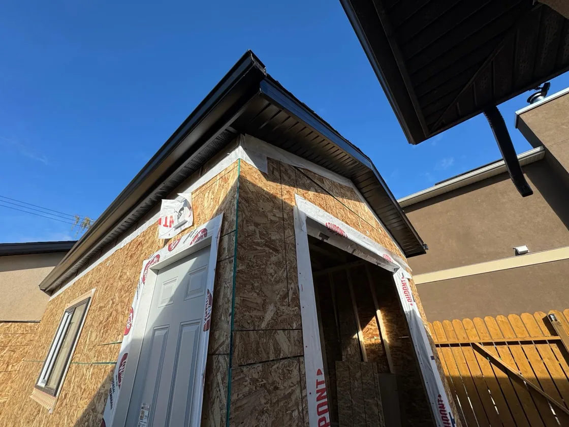 Dark gutters and soffit along a roof edge above exposed wall sheathing in Regina