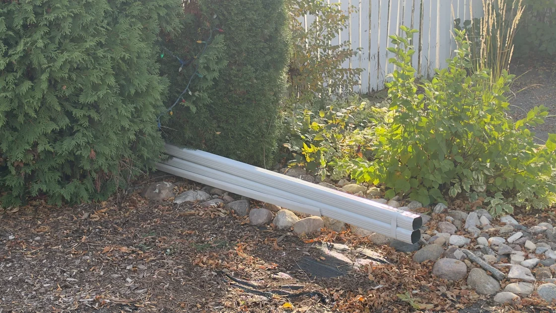 White downspout sections resting beside shrubs and a garden bed at a Regina property.
