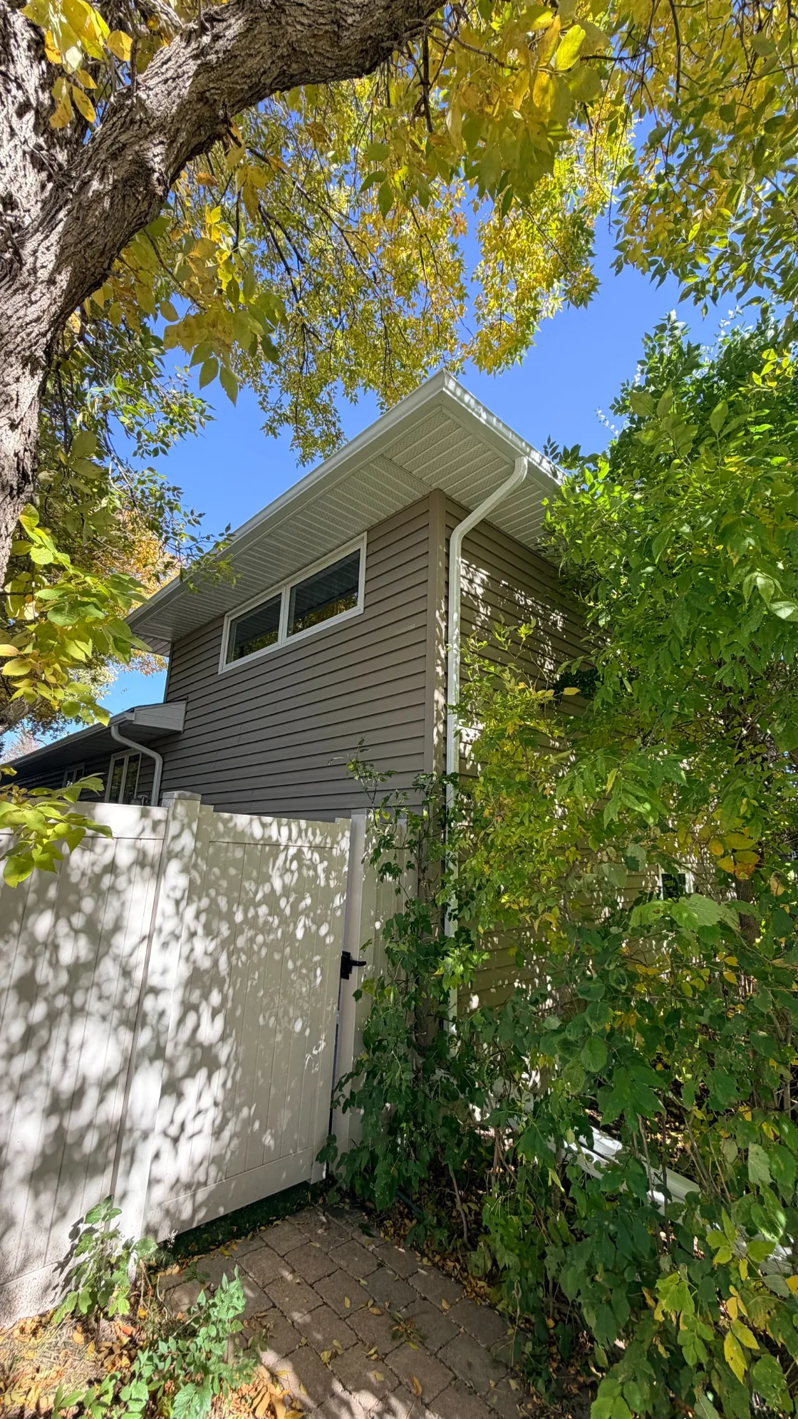 White gutter and downspout at the roof corner of a Regina home surrounded by trees