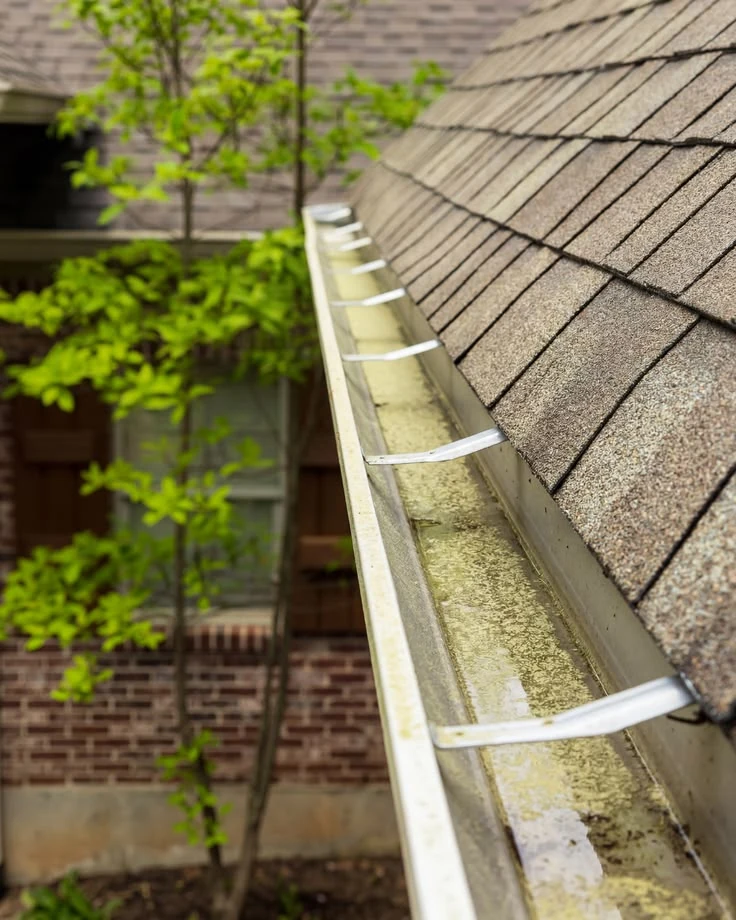 Open gutter with metal hangers beside a shingle roof