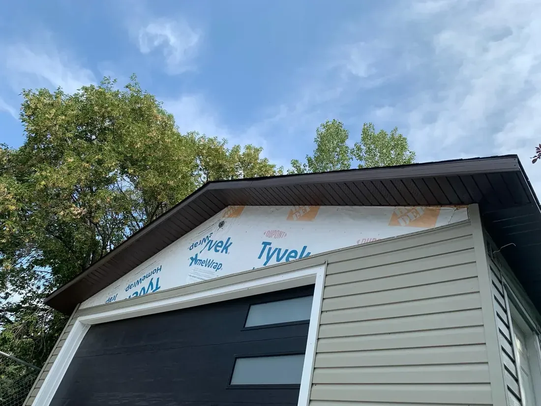 Siding installation in progress beneath a finished roof edge